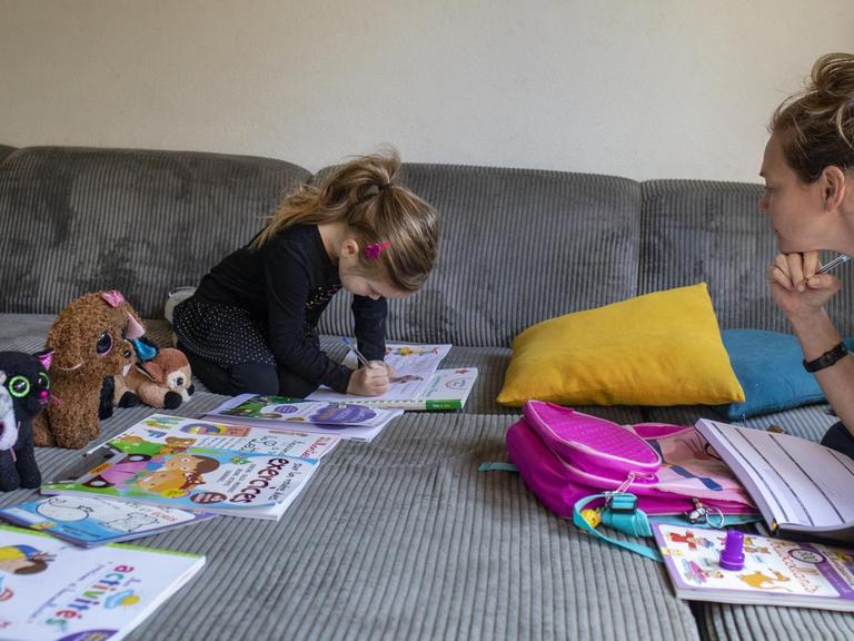 Abby, 6, mit ihrer Mutter Lisa beim Homeschooling auf dem Sofa zu Hause. Die Kuscheltiere sitzen auch alle vor einem Arbeitsheft. 20. März 2020 in Claira, Frankreich.