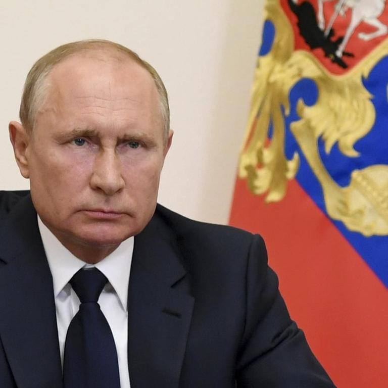 Der russische Präsident Wladimir Putin sitzt hinter einem Schreibtisch und blickt in die Kamera. Hinter ihm sind zwei Flaggen zu sehen.