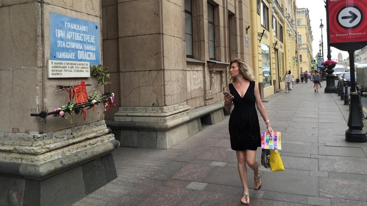 Eine Frau geht in St. Petersburg auf einer Straße an der Warntafel aus der Blockadezeit vorbei.