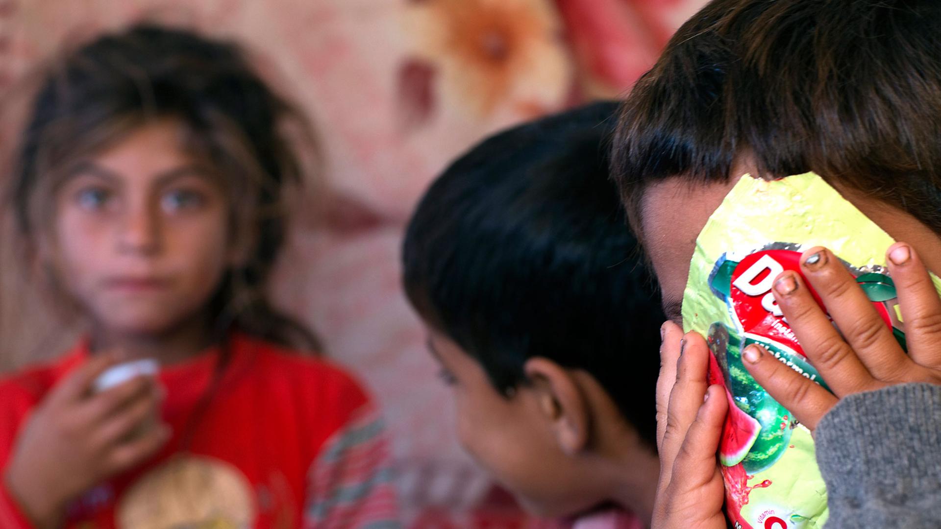 Drei Kinder einer syrischen Flüchtlingsfamilie, eines verdeckt sein Gesicht mit einer Tüte Bonbons.