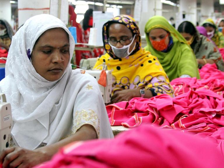 FRauen und Männer arbeiten unter schweren Bedingungen in der Textilfabrik 'One Composite Mills' in Gazipur an Nähmaschinen.