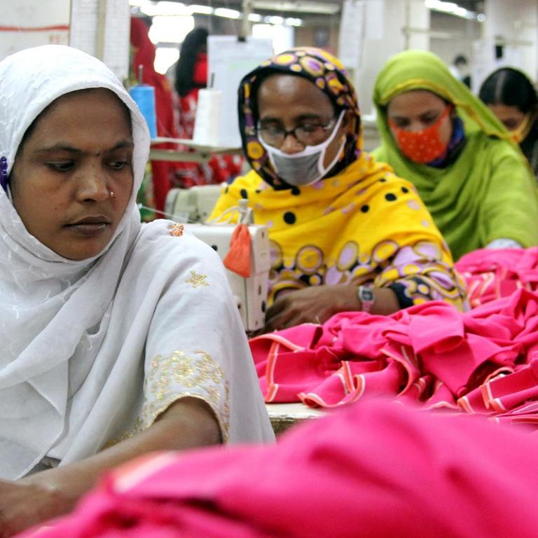 FRauen und Männer arbeiten unter schweren Bedingungen in der Textilfabrik 'One Composite Mills' in Gazipur an Nähmaschinen.