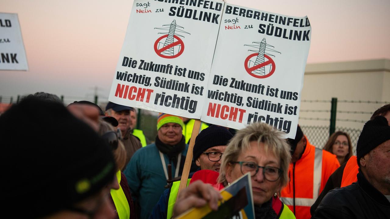 Stromtrassengegner halten vor dem neuen Umspannwerk Schilder mit der Aufschrift "Bergrheinfeld sagt Nein zu Südlink" in die Höhe.