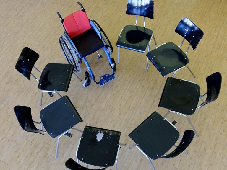 Ein Rollstuhl steht in einer Schule zwischen anderen Stühlen.