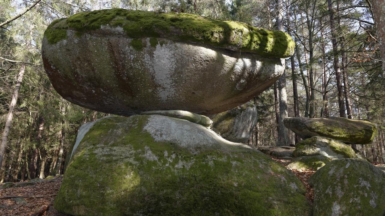 Zwei große Granitsteine liegen ausbalanciert aufeinander im Wald.