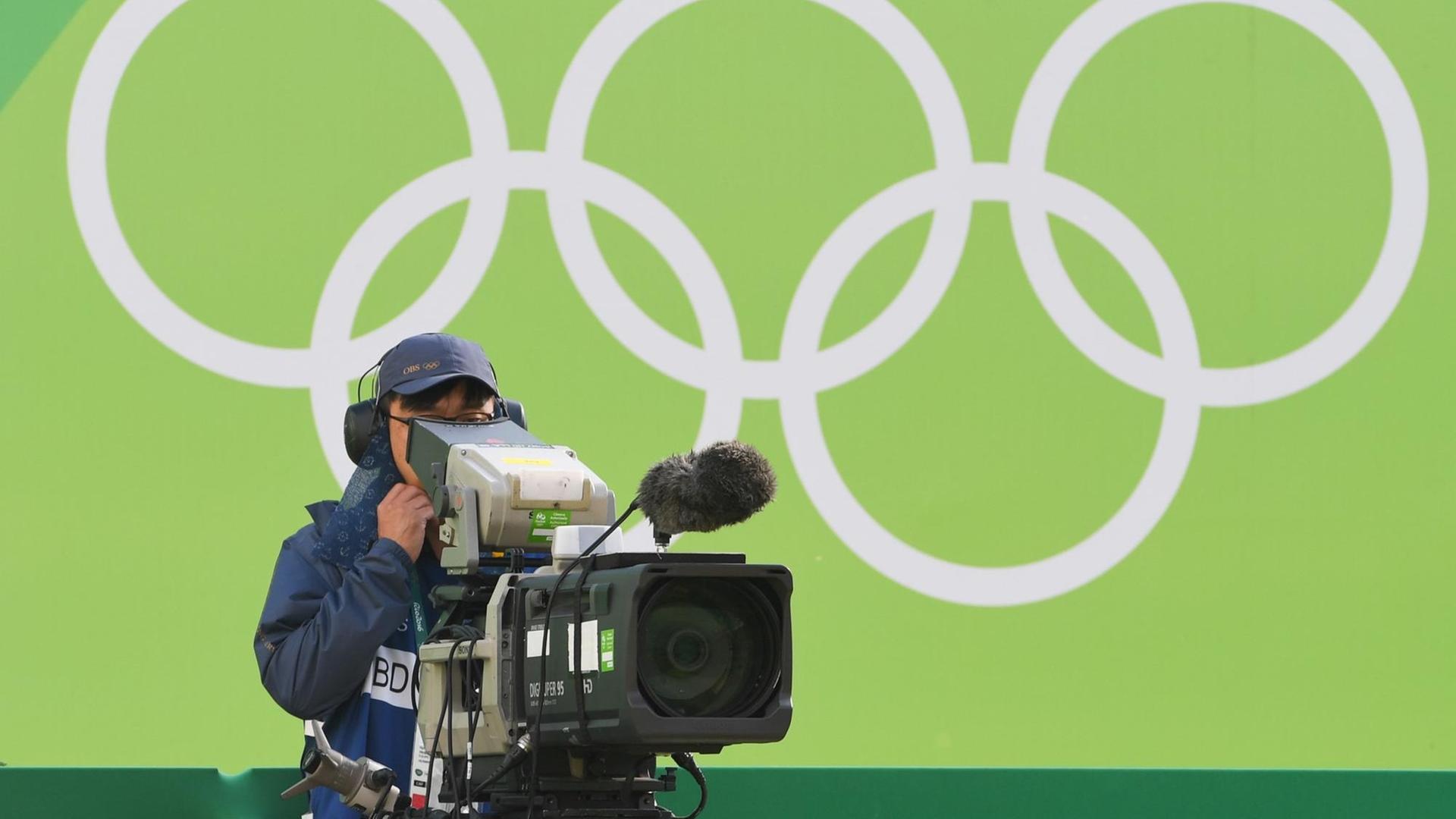 Ein Kameramann steht bei den Olympischen Spielen in Rio vor einer grünen Wand mit den Olympischen Ringen
