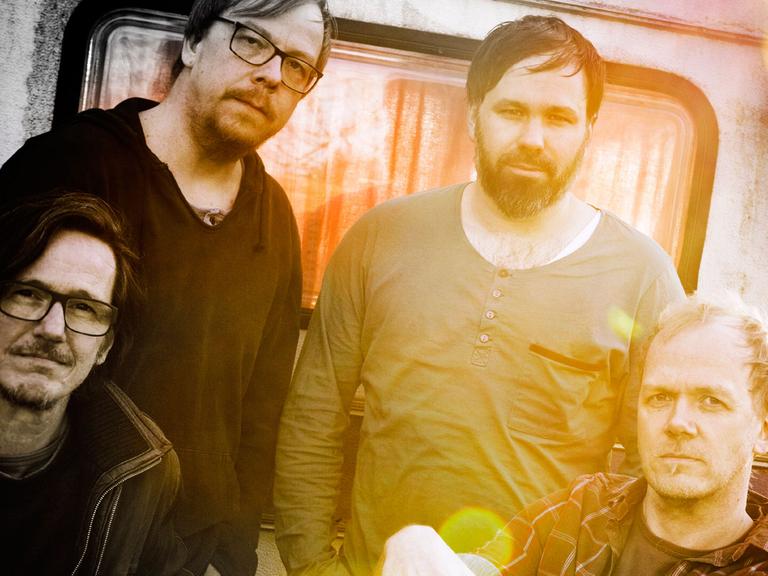 Die vier Musiker der Bremer Band Someday Jacob, in gelbliches Licht getaucht, vor einem Wohnmobil mit Patina