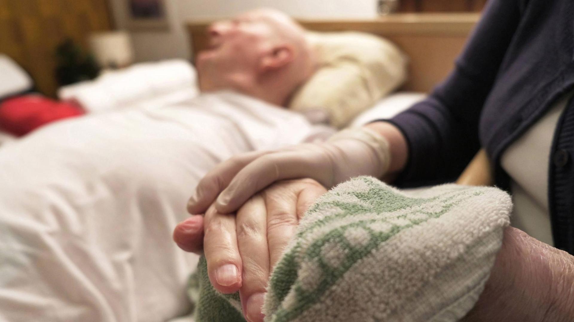 Eine Frau wäscht mit einem Lappen die Hand von einem älteren Mann
