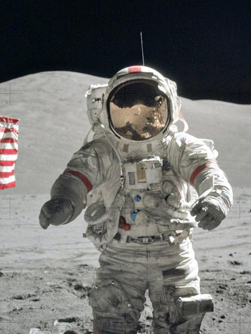 Der US-amerikanische NASA-Astronaut Eugene Cernan, Kommandant der Apollo 17, spaziert am 13. Dezember 1972 auf dem Mond herum. Im Hintergrund ist die US-Flagge zu sehen und eine Antenne.