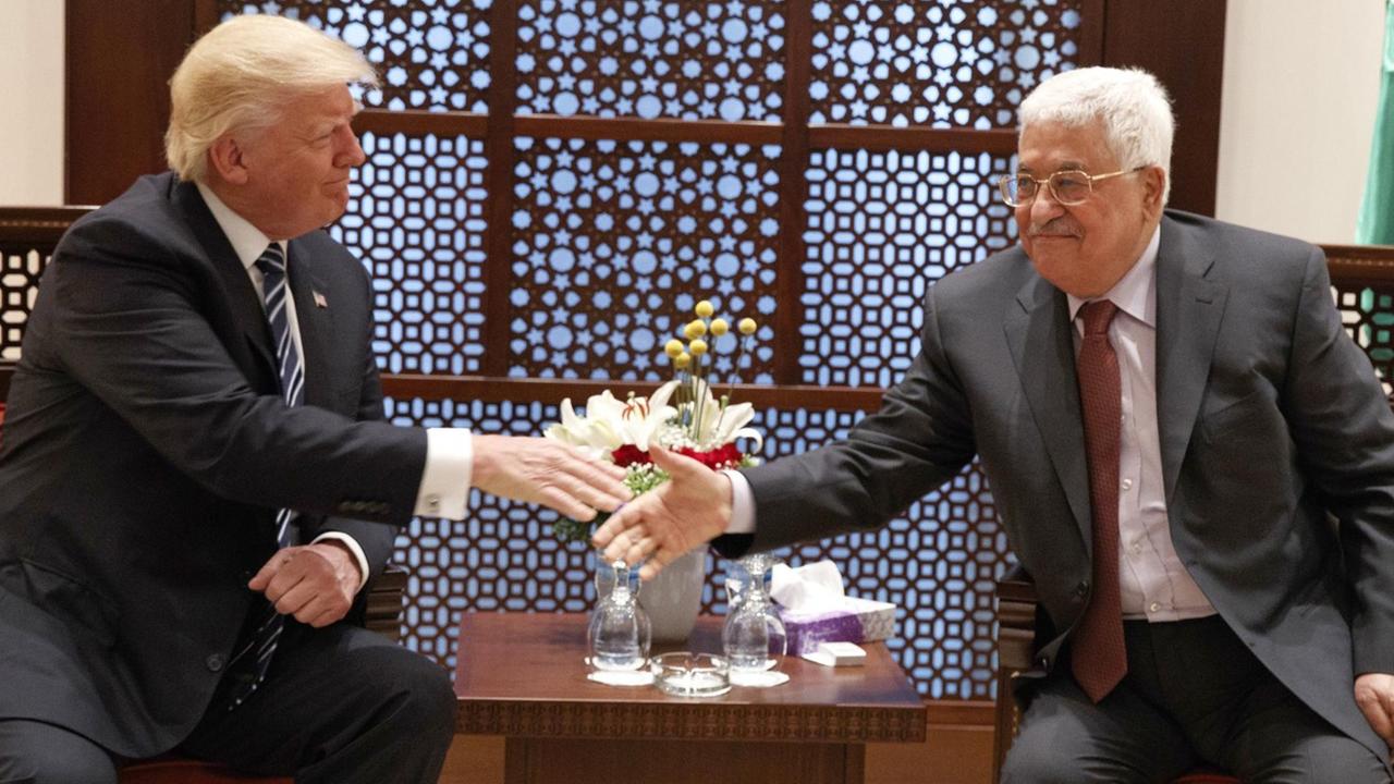 Trump und Abbas sitzen in Sesseln an einem kleinen Tisch und reichen sich lächelnd die Hand.