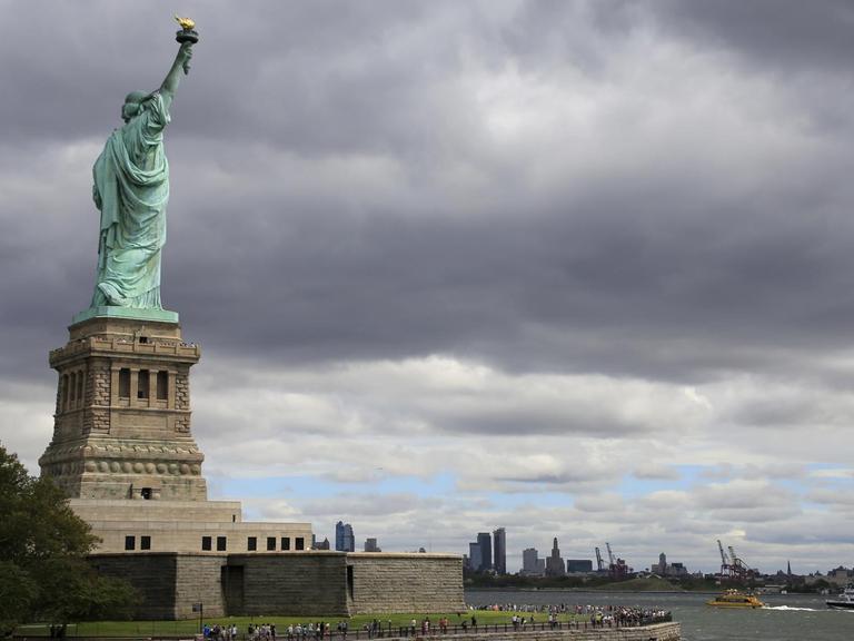 Die Freiheitsstatue auf Liberty Island auf ihrem Sockel, im Hintergrund angedeutet die Skyline von New York