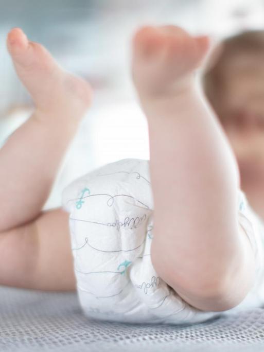 Ein Säugling trägt Pampers, während er auf einer Kommode liegt.