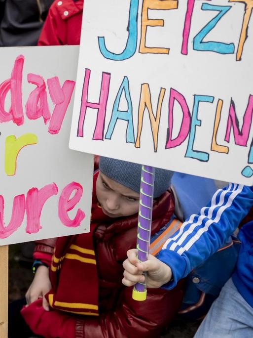 Drei junge Schulkinder zwischen sieben und acht Jahren demonstrieren am 22. März 2019 in Berlin im Rahmen der Proteste "Friday for Future". Sie halten ein Schild mit der Aufschrift "Jetzt handeln" nach oben.