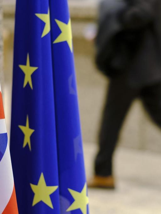 Die Fahnen Großbritanniens und der EU nebeneinander im Vordergrund, im Hintergrund ein laufender Mensch auf der Straße