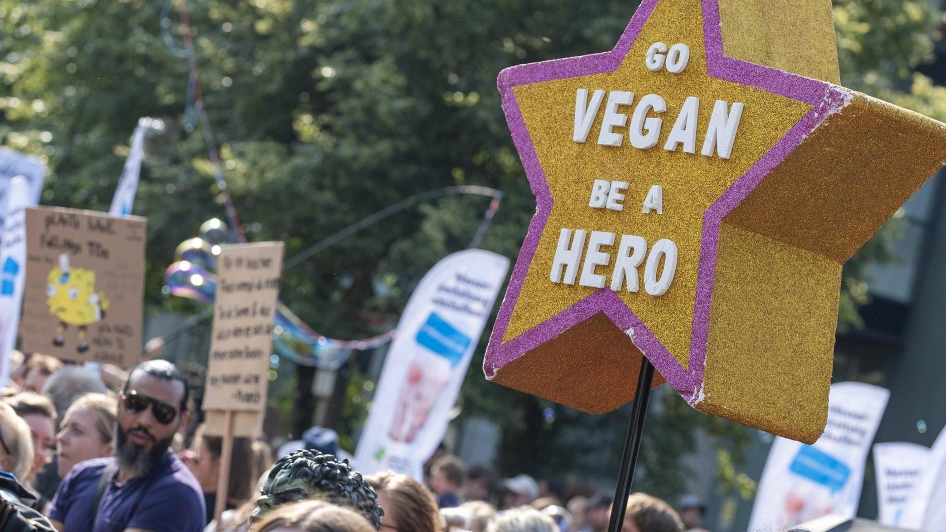 Menschen protestieren für mehr Tierschutz. Auf einem fünfzackigen Stern im Vordergrund steht: "GO VEGAN BE A HERO"