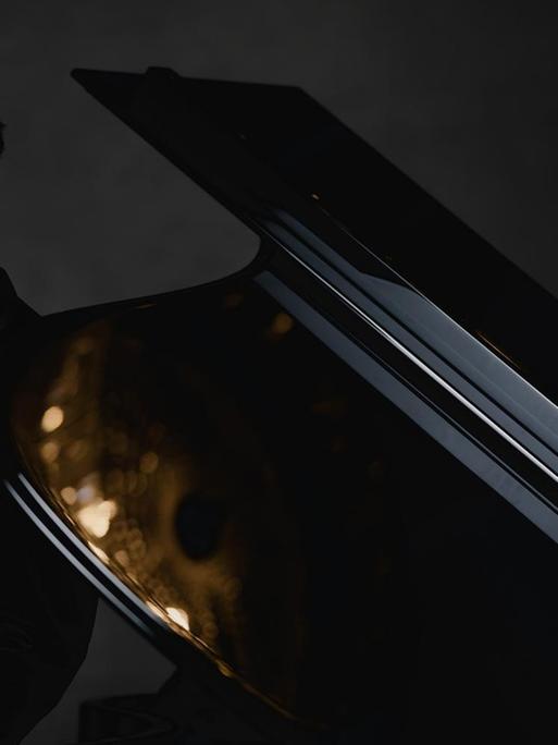 Der Pianist steht neben einem aufgeklappten Flügel, in dem sich goldene Lichter spiegeln.