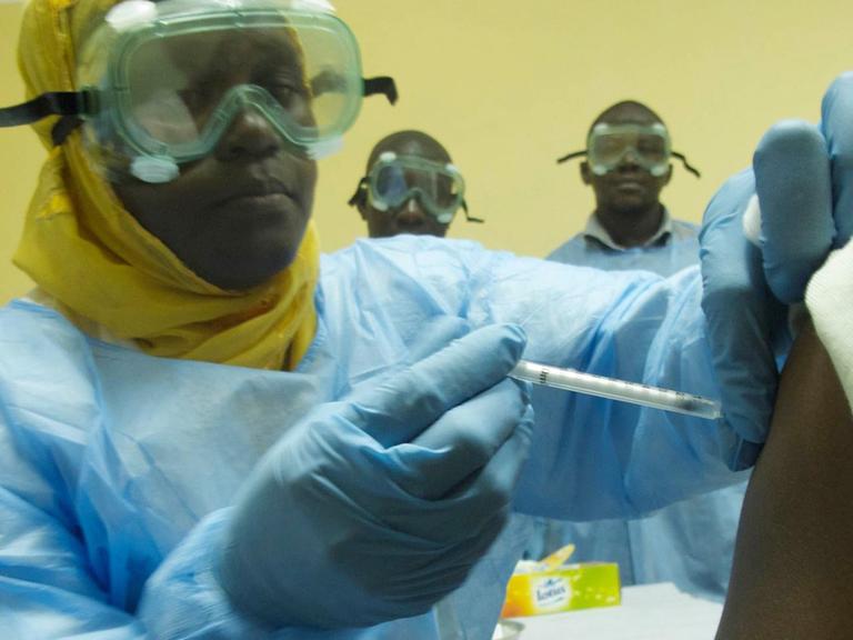 Ein afrikanischer Arzt in Schutzanzug verabreicht einem anderen Mann eine Spritze.