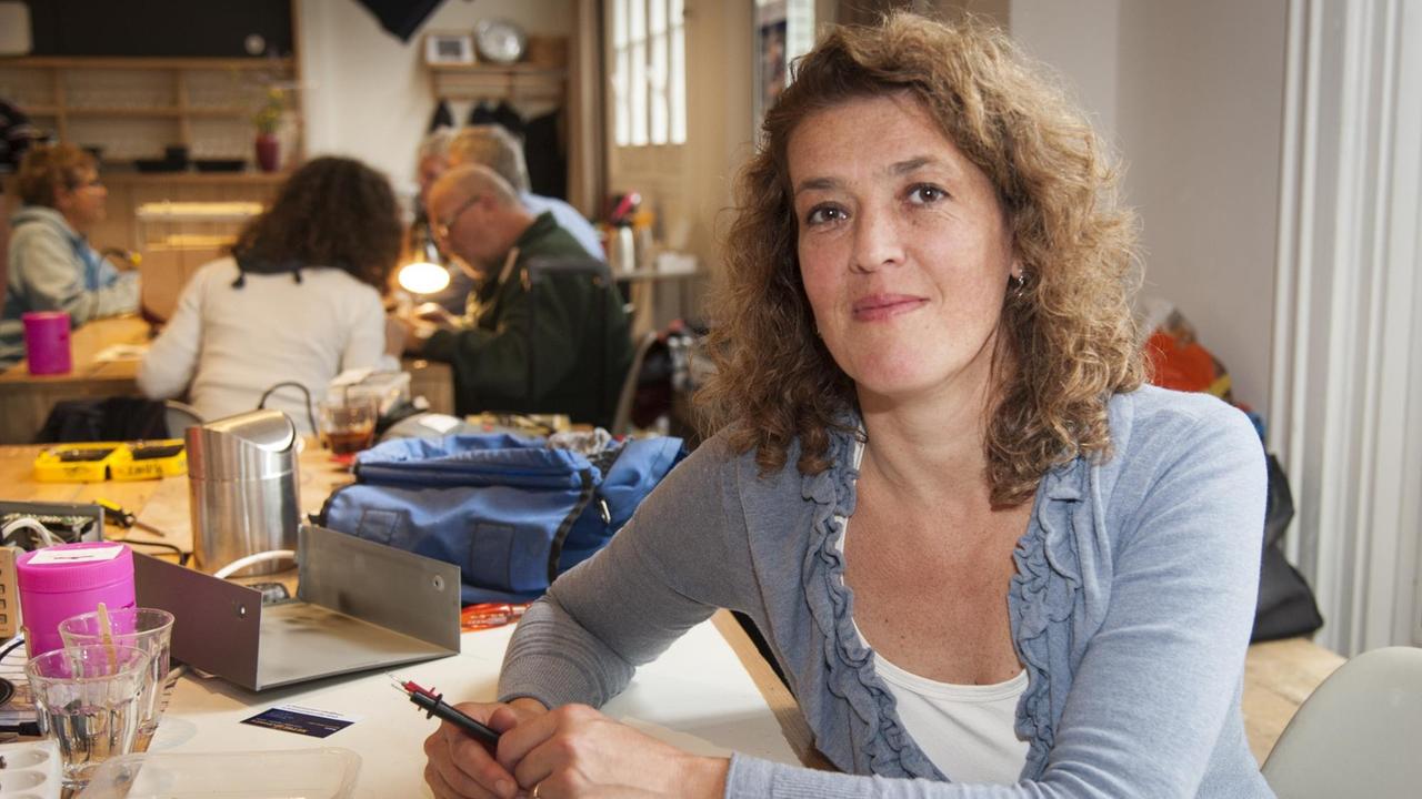 Martine Postma agiert seit 2009 als Gründerin der Repair-Café-Bewegung. Mittellange, lockige Haare. Sie sitzt in Amsterdam in einem Repair-Café.