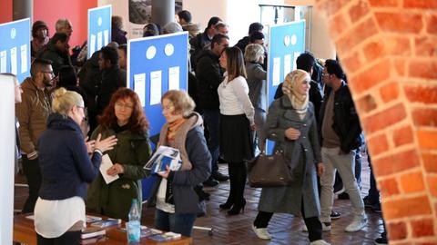 Halle mit Ständen von Arbeitgebern, dazwischen Menschen.