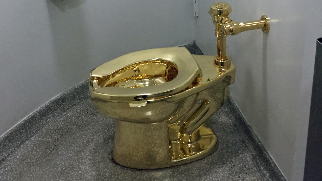 Die Toilette steht in einem kleinen Raum und ist an die Wand angeschlossen.