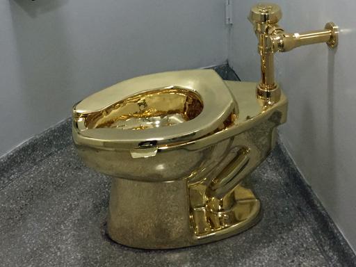 Die Toilette steht in einem kleinen Raum und ist an die Wand angeschlossen.