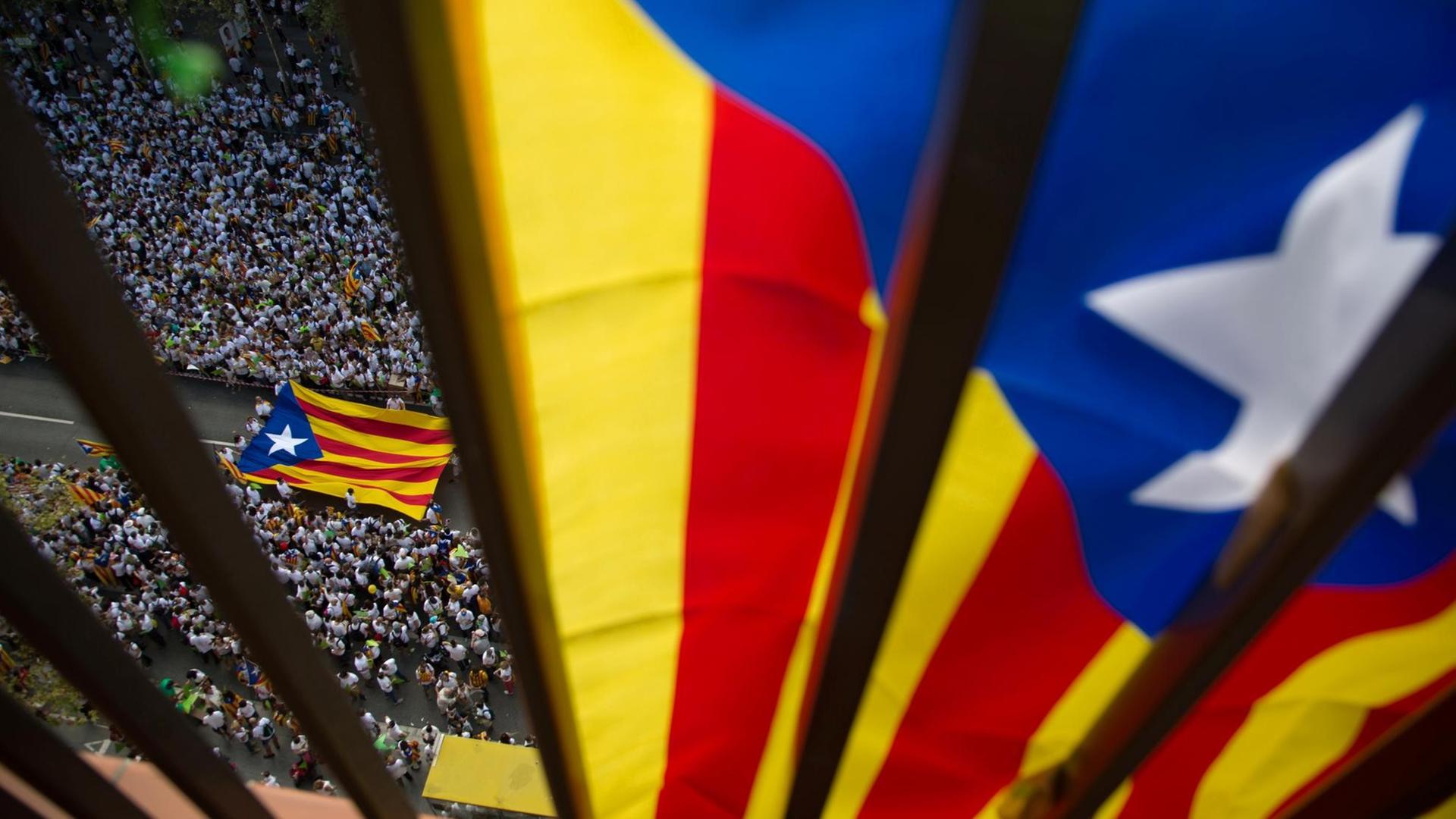 Barcelona am Nationalfeiertag Kataloniens. An einem Balkon hängt die katalanische Flagge, unterhalb des Balkons auf der Straße ziehen Menschen mit der Flagge durch die Straße.