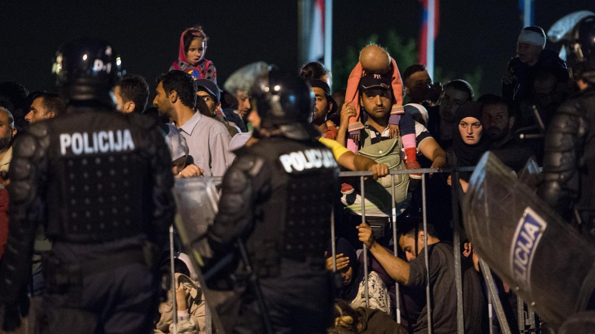 Flüchtlinge stehen am 19.09.2015 an der Grenze in Bregana zwischen Kroatien und Slowenien hinter einem Absperrgitter, davor stehen slowenische Polizisten.