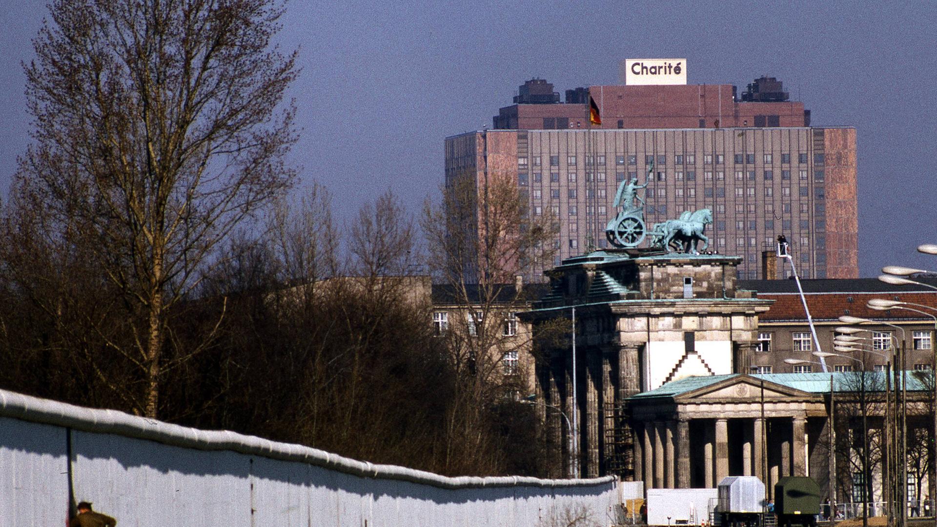 Ein Grenzsoldat schaut nahe dem Brandenburger Tor durch die Berliner Mauer nach West-Berlin
