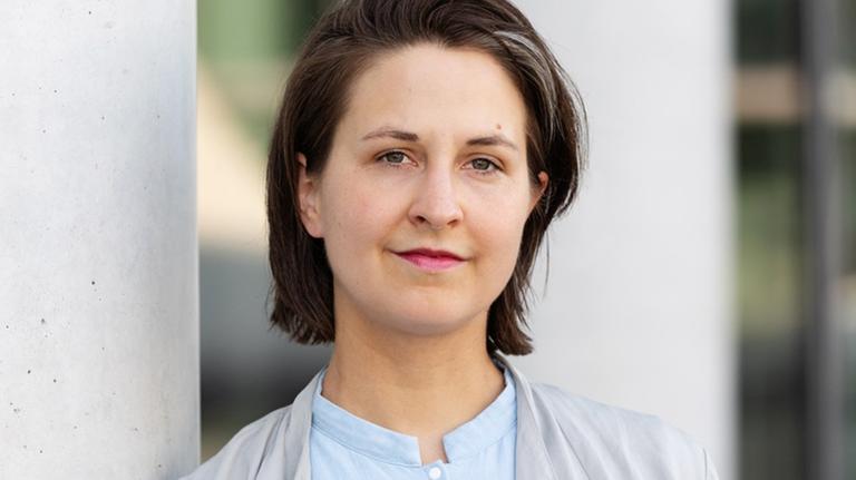Die Rechtsphilosophin Dana Schmalz lehnt an einem Betonpfeiler und schaut freundlich in die Kamera.