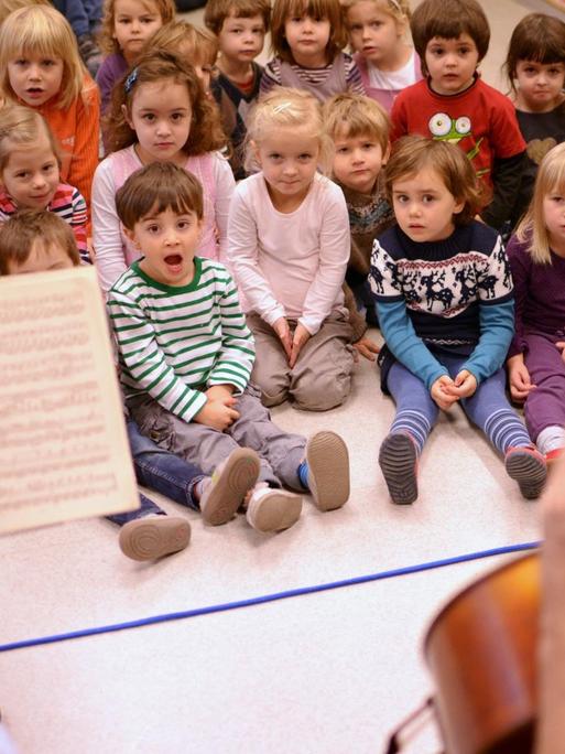 Kinder sitzen singend zwei Cellisten gegenüber.