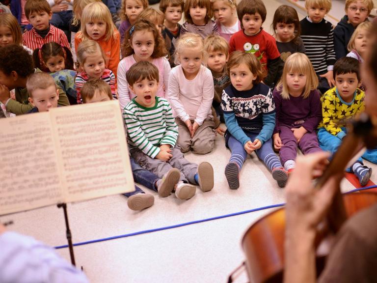 Kinder sitzen singend zwei Cellisten gegenüber.