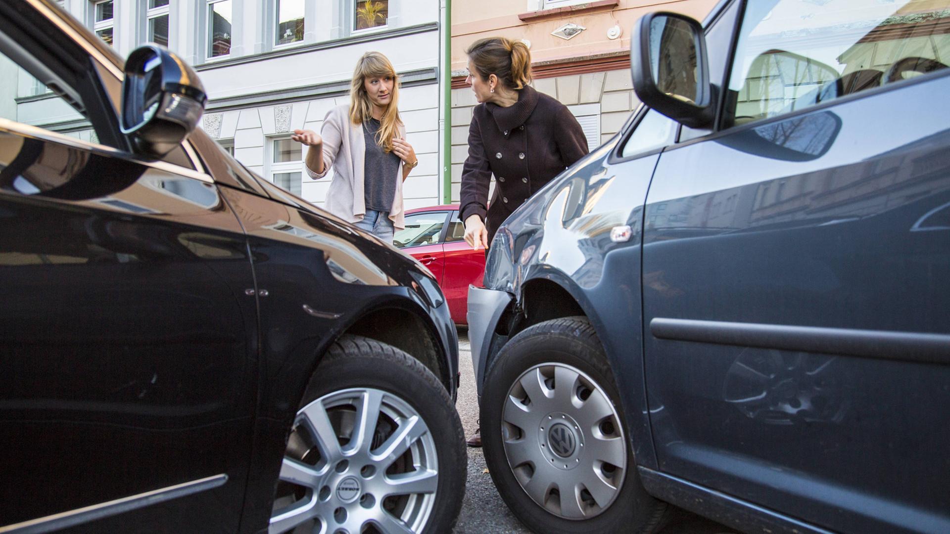 Zwei Frauen stehen diskutierend vor ihren beschädigten Autos.