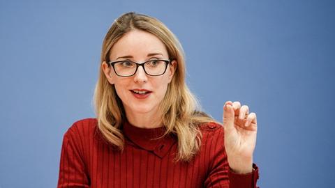 Eine blonde Frau mit eckiger Brille gestikuliert fein beim Reden. Sie trägt 