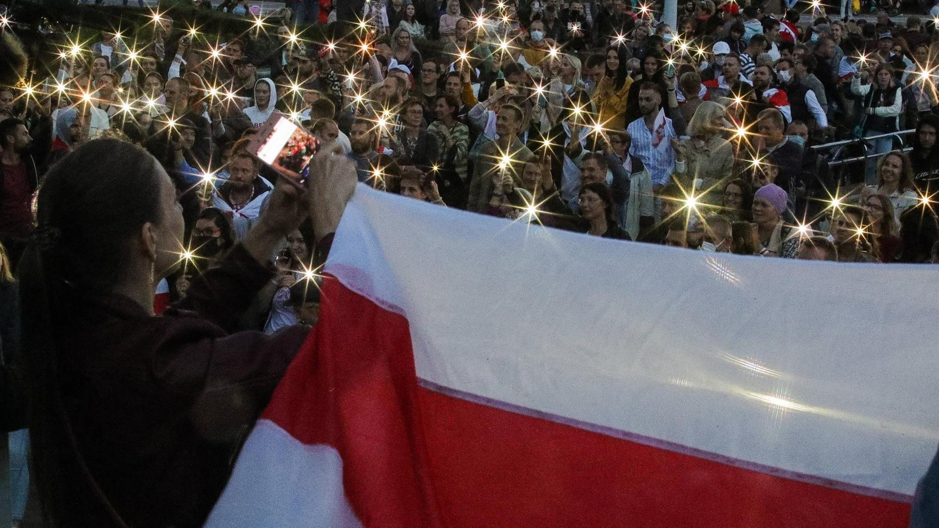 Ein belarussische Flagge vor Demonstrierenden mit leuchtenden Handys.