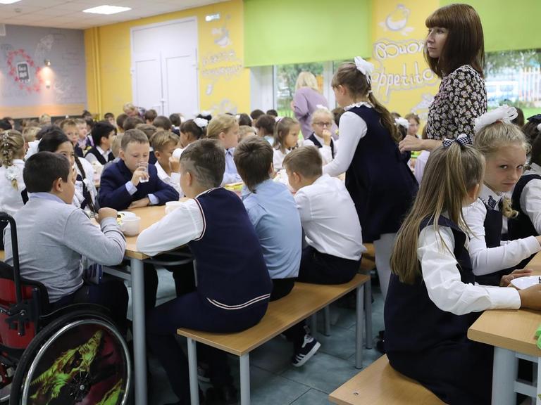 Schüler und Schülerinnen einer Moskauer Schule sitzen zusammen in der Kantine beim MIttagessen, unter ihnen auch ein Kind im Rollstuhl.