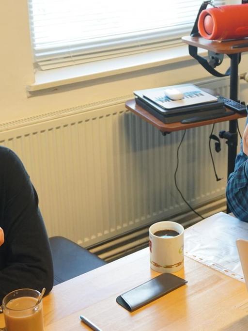 Die Mitarbeitenden des Mehrgenerationenhauses Wassertor, Ralf Pierau und Vicdan Avci sitzen am Tisch und halten Smartphones in der Hand. Darüber kommunizieren sie mit Senioren, die wegen Corona nicht mehr in die Einrichtung kommen können.