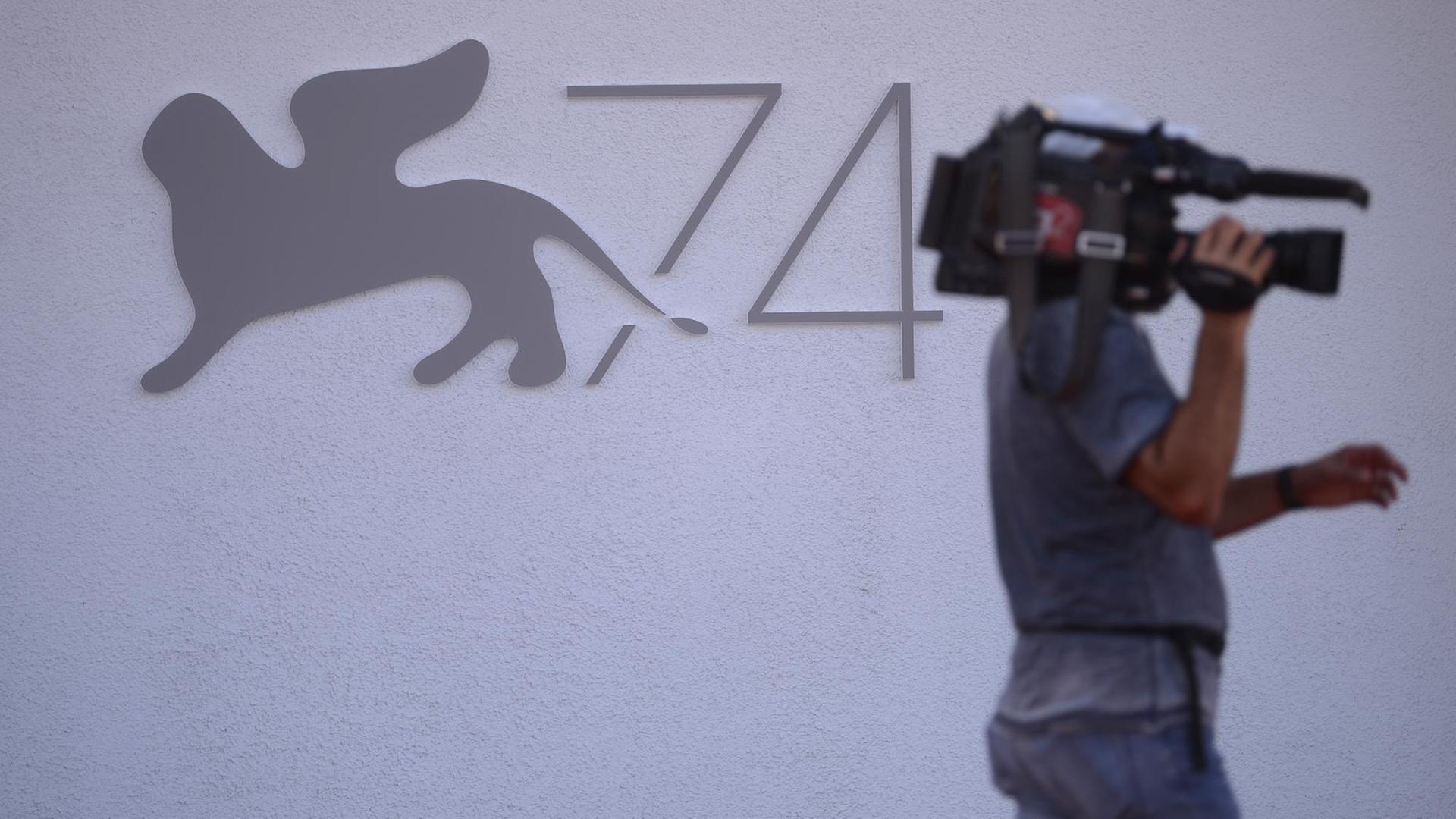 Ein Kameramann läuft am Logo der Filmfestspiele mit dem Goldenen Löwen vorbei