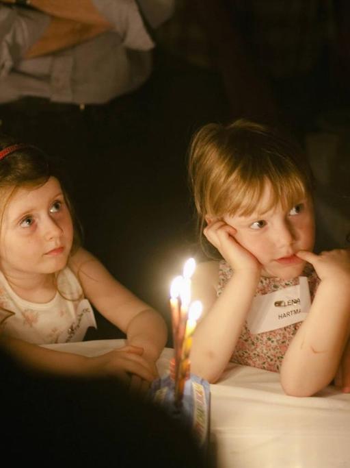 Kinder sitzen um einen Tisch und beobachten, wie die Kerzen zum jüdischen Lichterfest Chanukka angezündet werden.