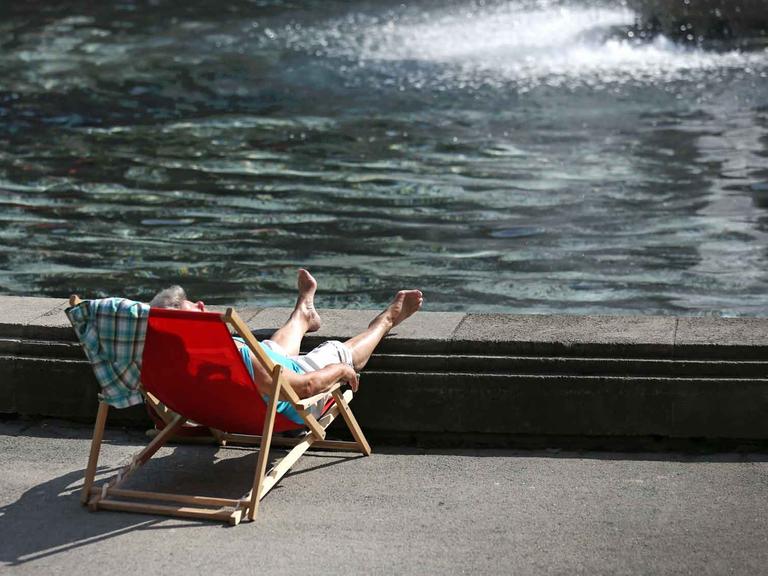 Eine Frau sonnt sich in einem Liegestuhl am Springbrunnen des Museum Kunstpalast in Düsseldorf