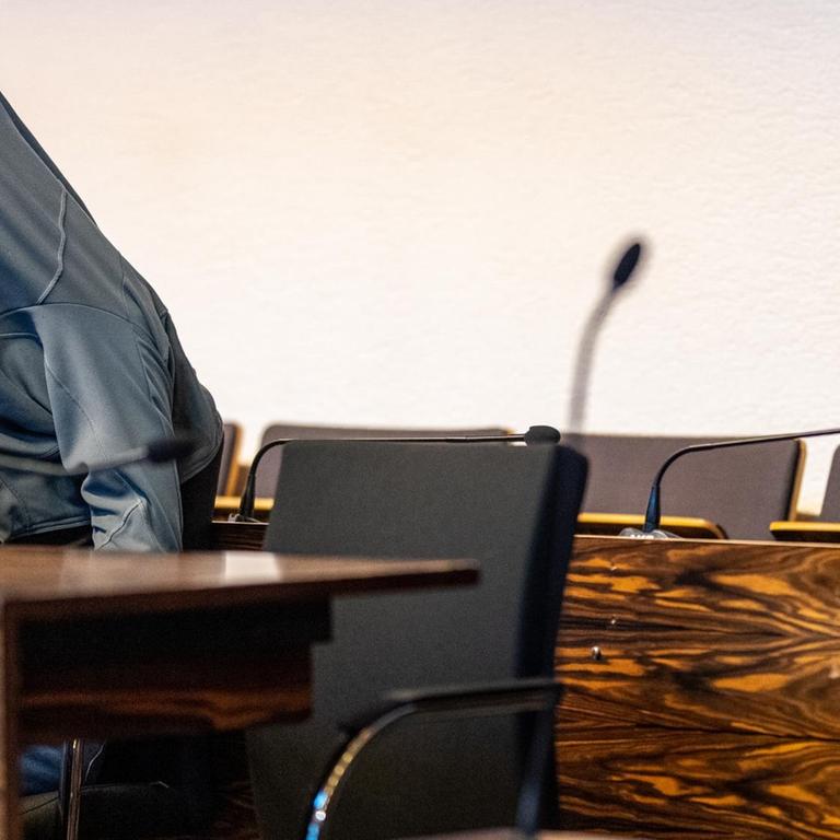 Der Angeklagte sitzt am linken Bildrand an einem Tisch, er hat sich die Jacke über den Kopf gezogen.