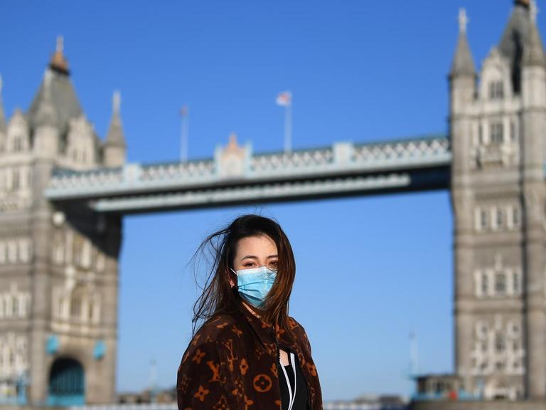 Ein Frau mit Maske posiert für ein Foto vor der Tower Bridge in London, England.