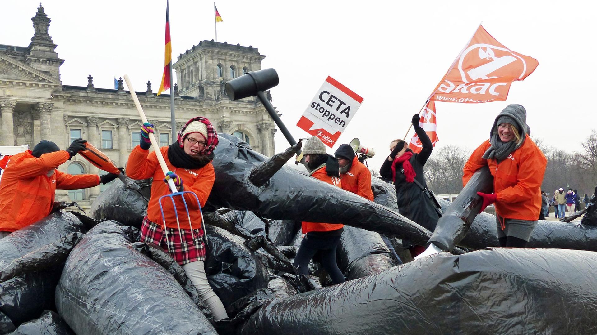 Mehrere Aktivisten von Attac kämpfen vor dem Berliner Reichstagsgebäude mit einem Monster und halten Protestplakate.