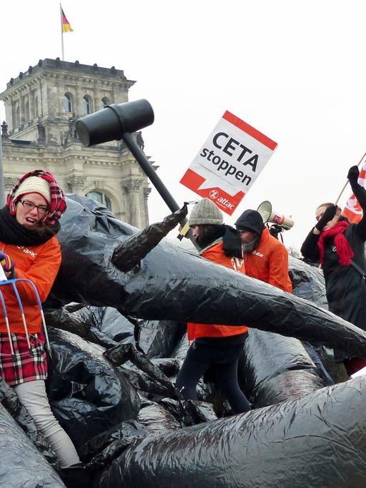Mehrere Aktivisten von Attac kämpfen vor dem Berliner Reichstagsgebäude mit einem Monster und halten Protestplakate.