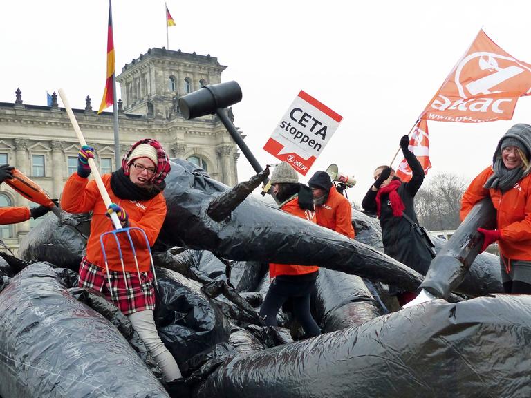 Mehrere Aktivisten von Attac kämpfen vor dem Berliner Reichstagsgebäude mit einem Monster und halten Protestplakate.