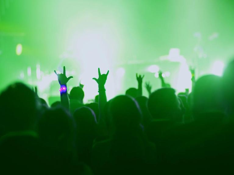 Eine in grünes Licht getauchte Bühne. Davor steht Publikum und einzelne Hände ragen in die Luft.