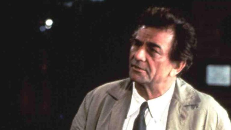 Schauspieler Peter Falk trägt als Inspector Columbo einen der für die Rolle typischen Trenchcoats. Er steht draußen im Dunkeln.
