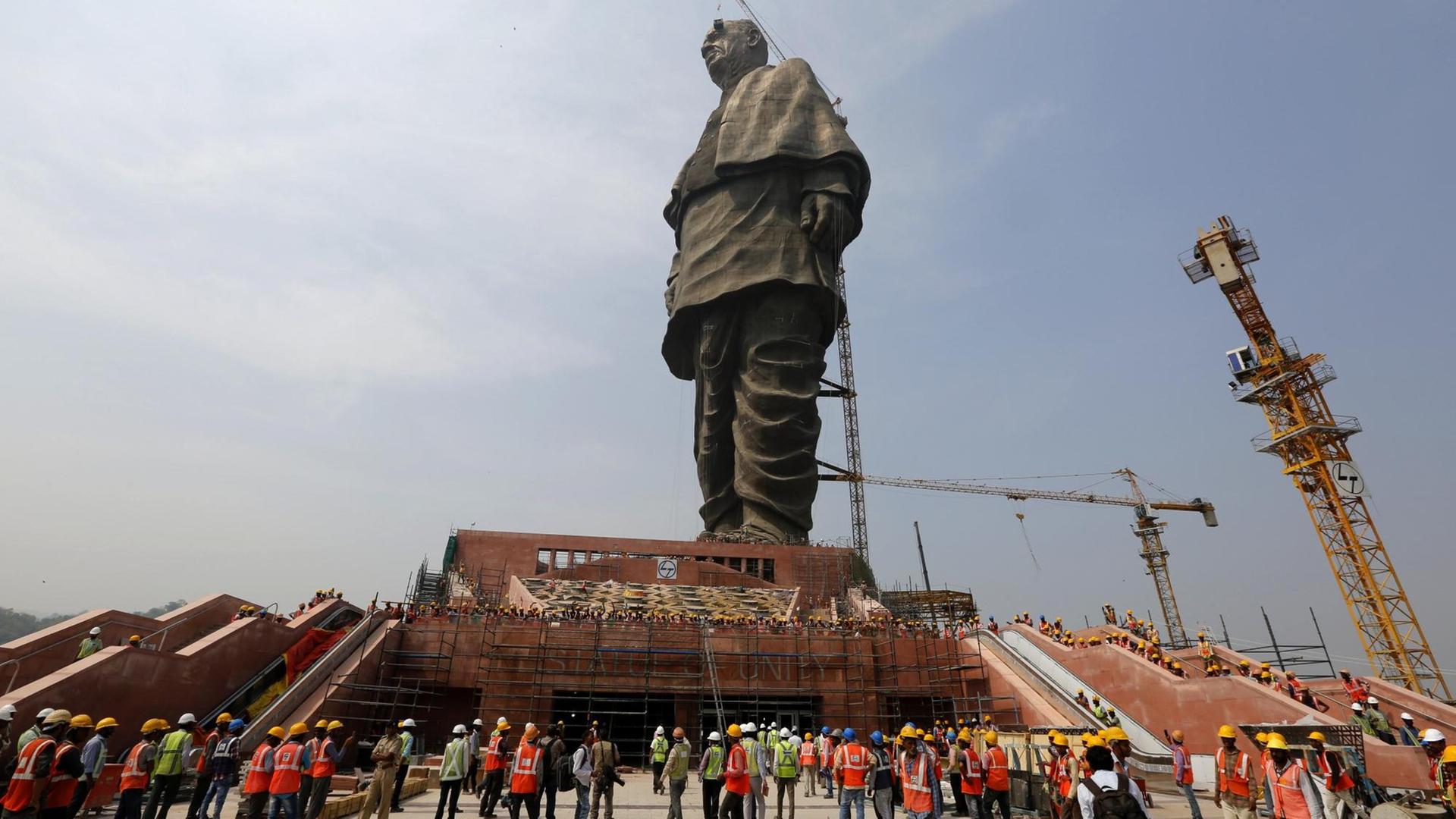 Indische Arbeiter vor einem riesigen Denkmal.
