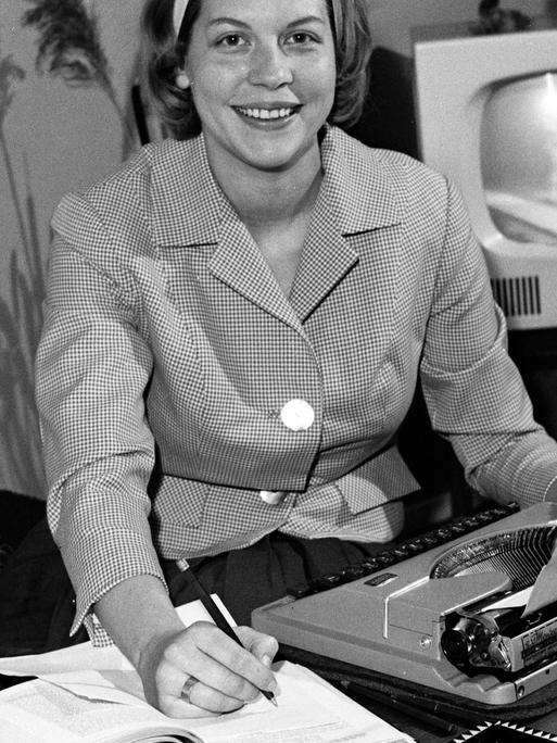 Homeoffice historisch: Eine junge Frau sitzt am Wohnzimmertisch mit Schreibmaschine und aufgeschlagenen Büchern, Deutschland 1960er Jahre.