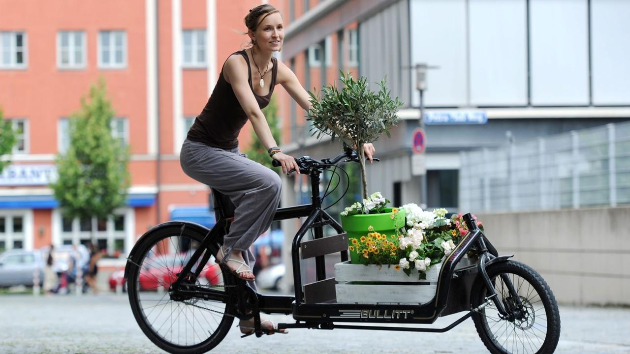 Eine Frau fährt mit einem Transportrad, das mit Blumen beladen ist, durch die Stadt.