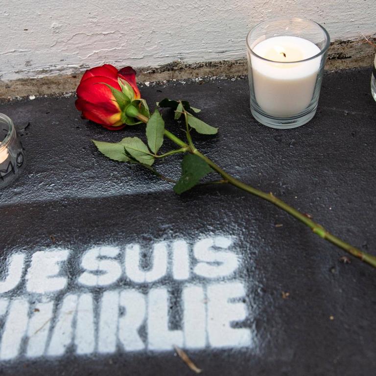 Eine Rose und Kerzen stehen auf der Straße, darunter der Schriftzug "Je suis Charlie".